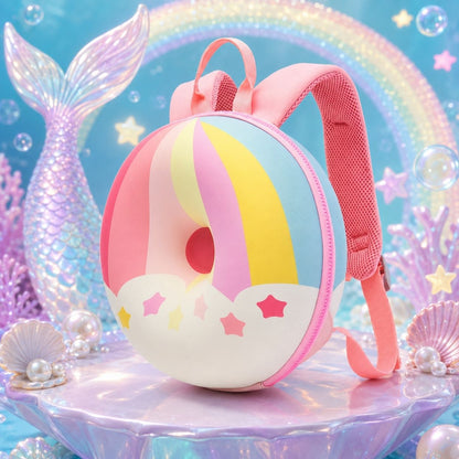 A pastel donut-shaped backpack with pink straps, decorated with pink, yellow, blue, and white stripes and star accents, set against a mermaid-themed background with a mermaid tail, bubbles, and shells.